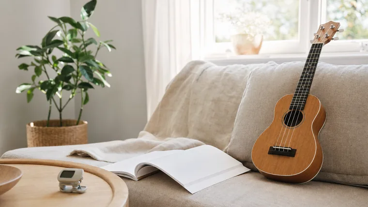 Sopranukulele på en soffa vid ett fönster med en uppslagen ackordbok och en stämapparat bredvid.